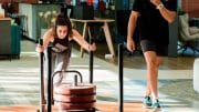 trainer watches girl pushing weights